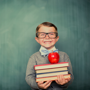 boy wearing bow tie holding stack of books and an apple